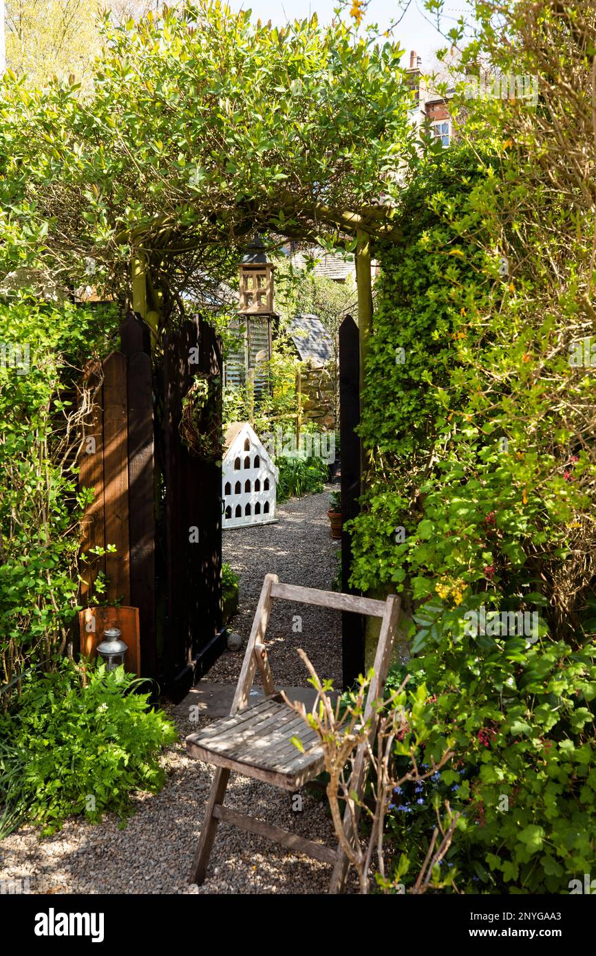 Looking through a garden gate with wooden seat outside, with arch covered in honeysuckle and plants, Appleby in Westmorland Eden Valley Cumbria Stock Photo