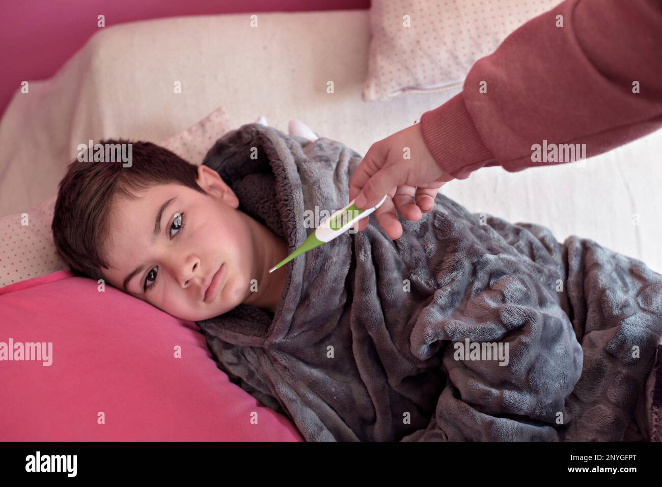 Sick boy with thermometer laying in bed and mother hand taking