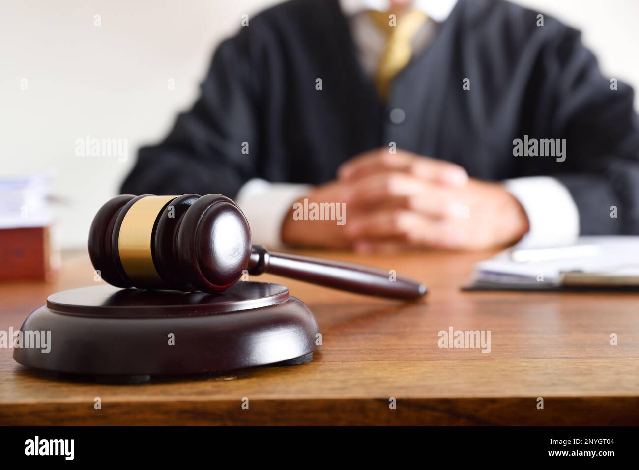 Detail of gavel and judge dressed in the toga sitting in the background on wooden table. Front view Stock Photo