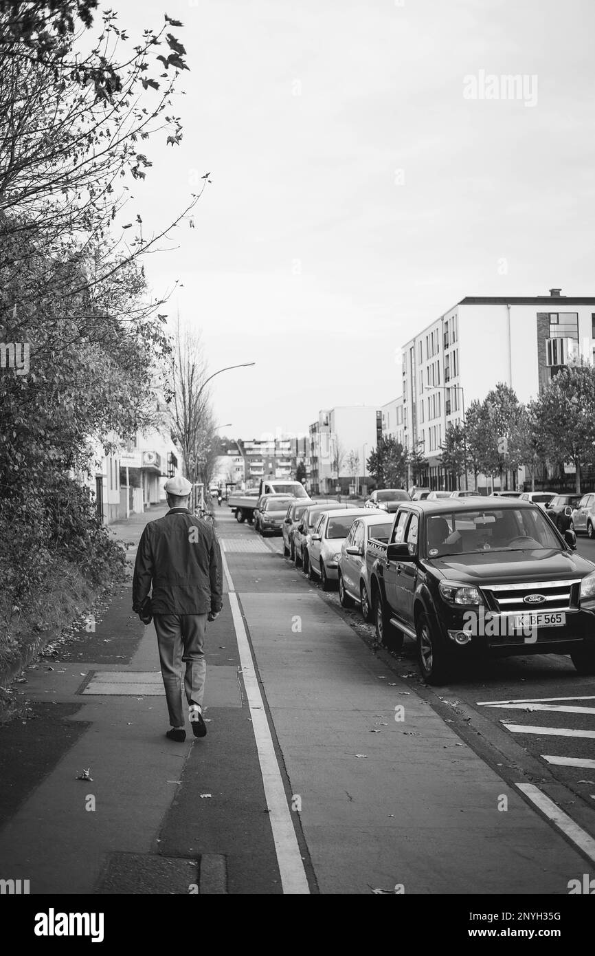 A black and white shot of an old man walking across the street. Street photography shows an everyday situation in the city. Stock Photo