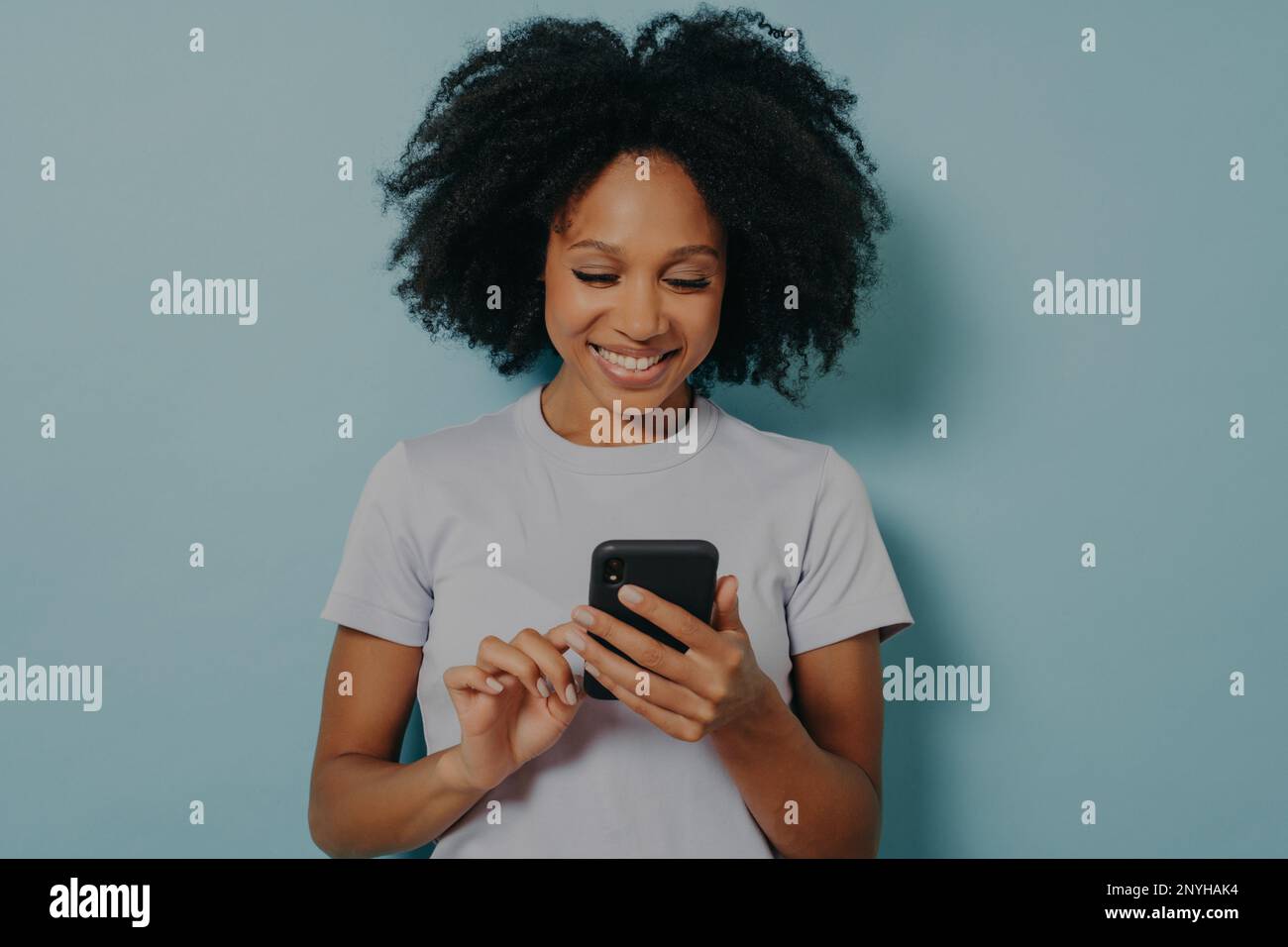 Pretty curly hair woman holds modern mobile phone, types messages on smartphone device, enjoys online communication, downloads special app for chattin Stock Photo