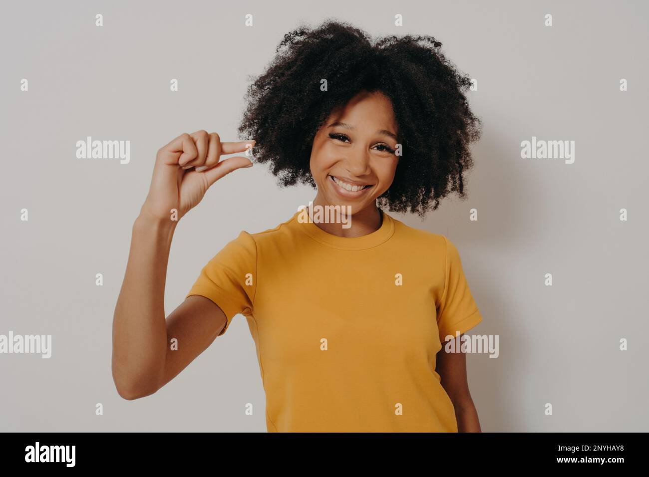 Cheerful smiling African American woman gestures small size with fingers, asks for little bit time, or measures too small object, shows something mini Stock Photo