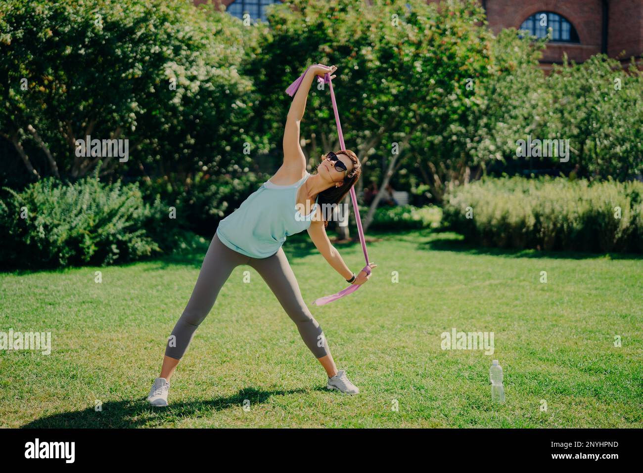 Full length shot of active woman stretches arms with fitness gum has