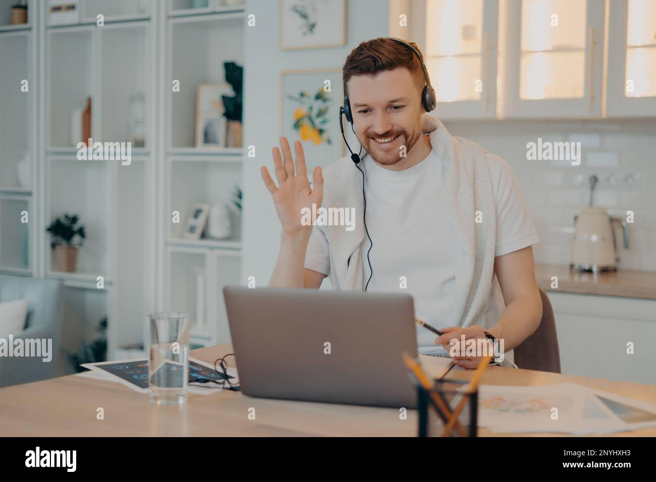 Smiling man freelancer in headphones waving to his colleague and having ...
