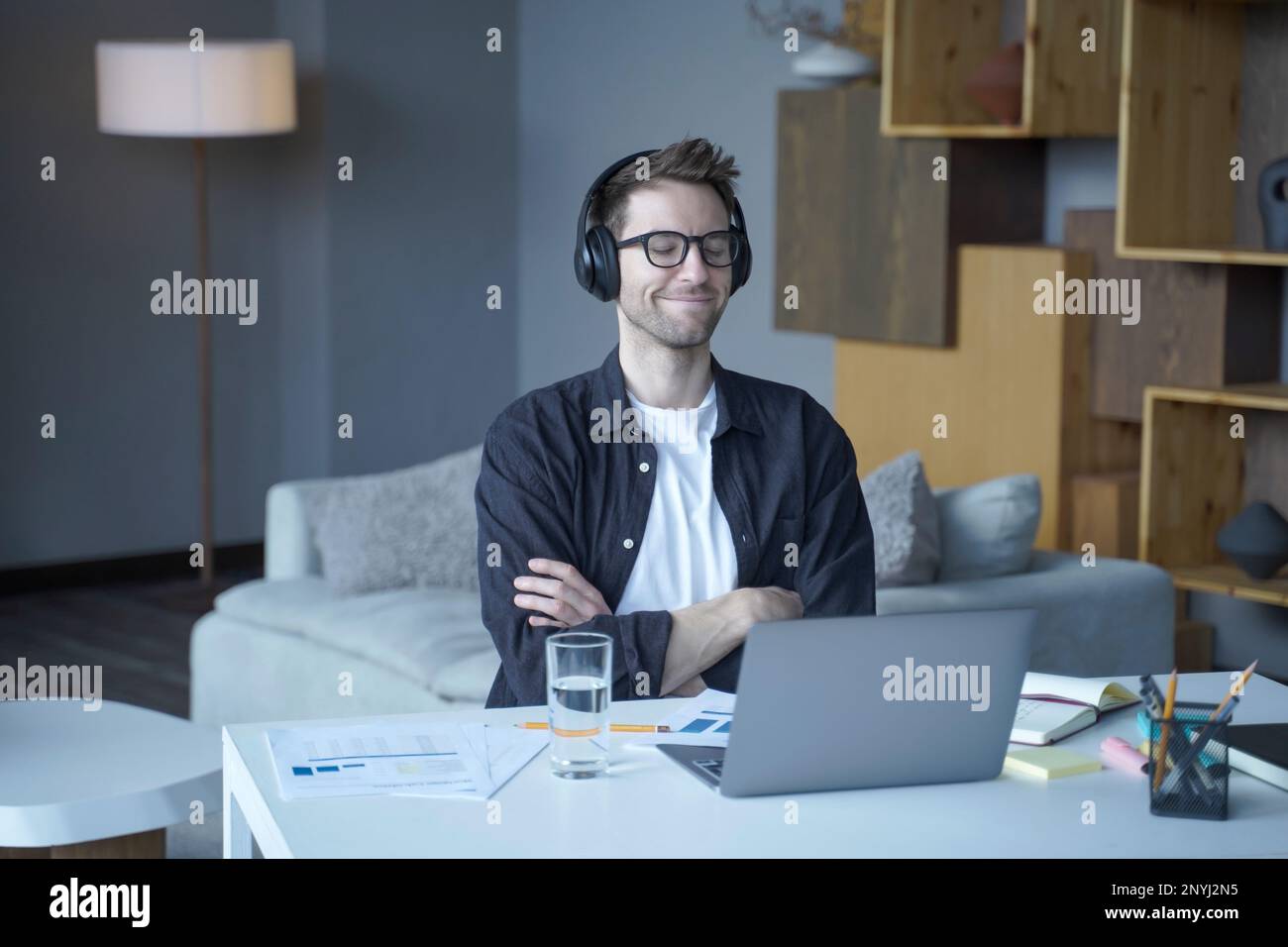 Young smiling happy austrian male freelancer sitting with closed eyes in headphones and enjoying listening to music at home office, man listens podcas Stock Photo