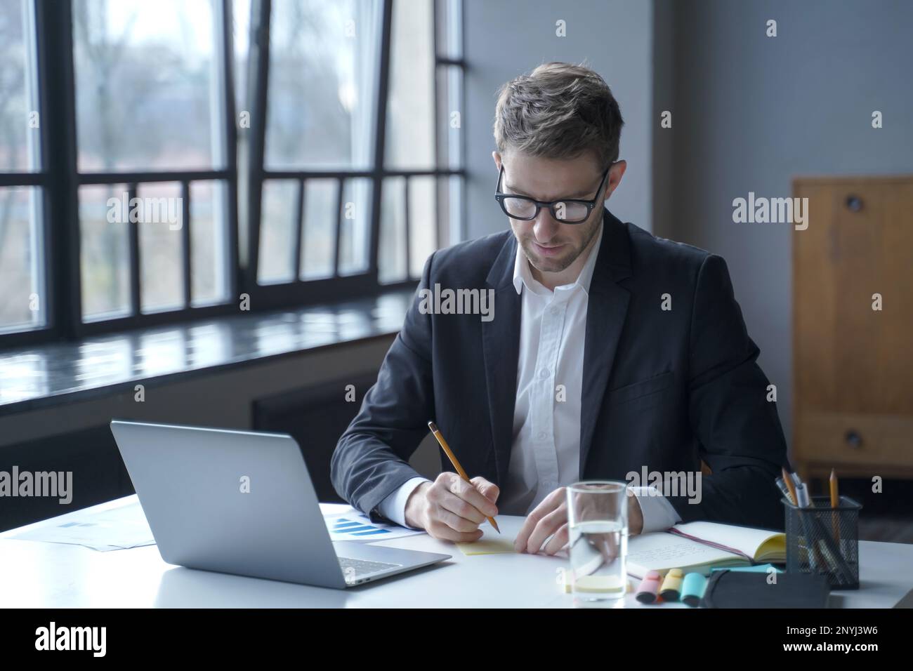 Immersed in work. Focused young German male banker writes down memos on sticky notes to remember important details to share for upcoming online meetin Stock Photo