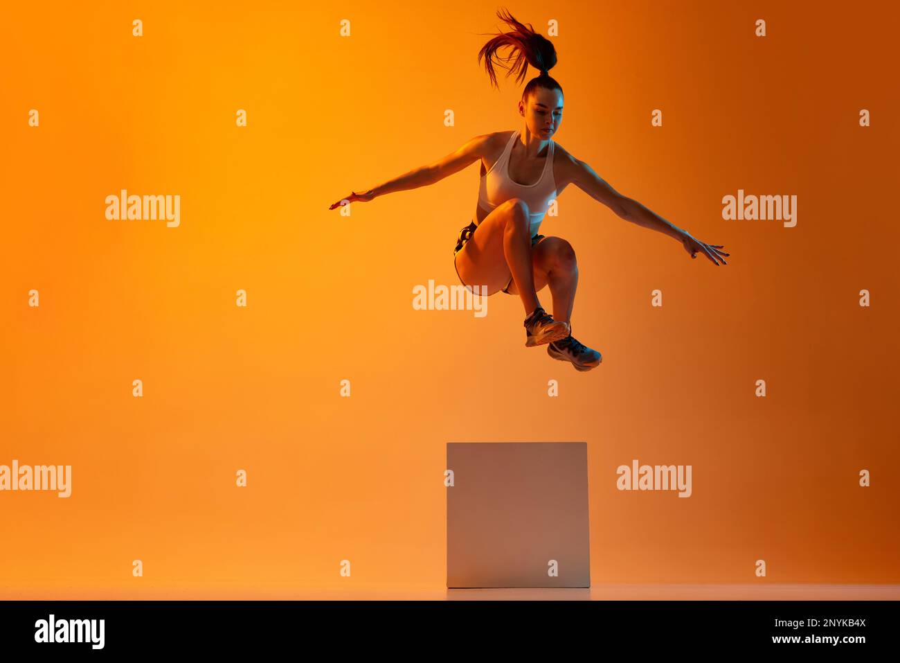 Workout. Young sportive girl, athlete training, jumping over block