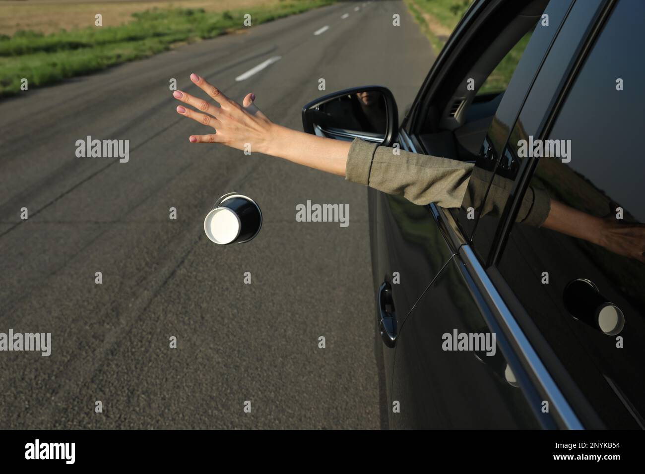Driver throwing away paper cup from car window. Garbage on road Stock