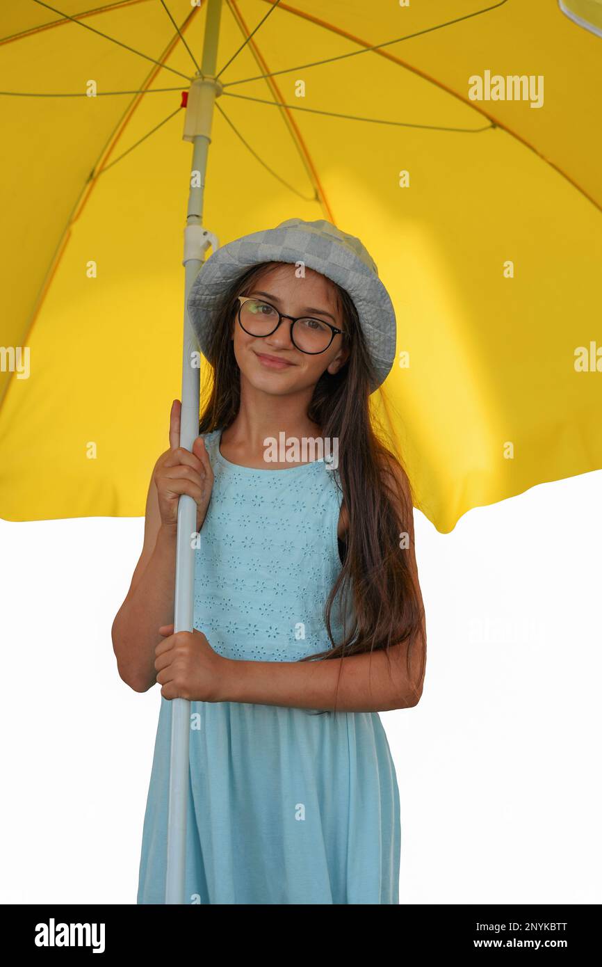 Little girl under an umbrella isolated on white background. A cute girl in a turquoise dress under a large yellow umbrella. A child with long dark hai Stock Photo
