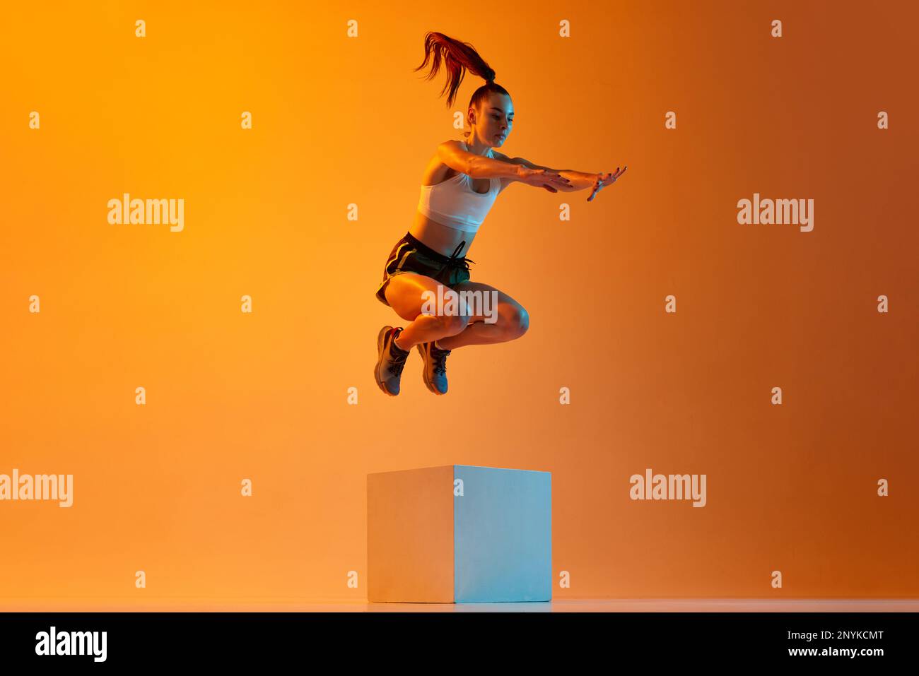 Strong body. Young sportive girl, athlete training, jumping over block