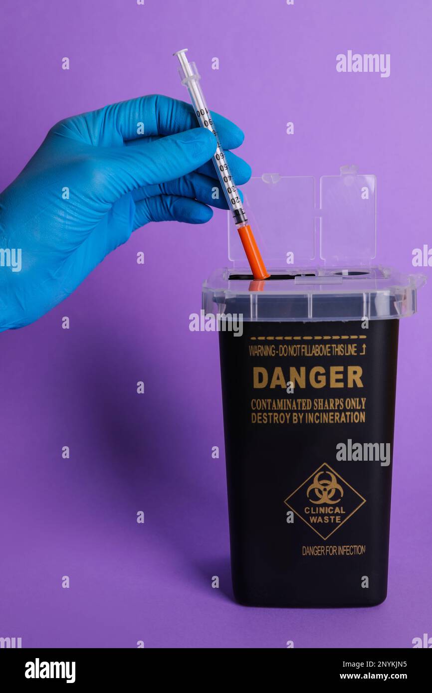 Doctor throwing used syringe into sharps container on violet background