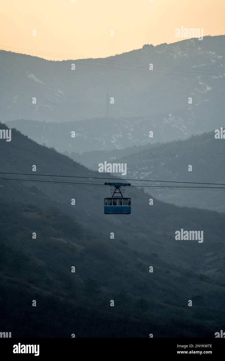 Blue old cabin of cable car moves against backdrop of crested mountains ...