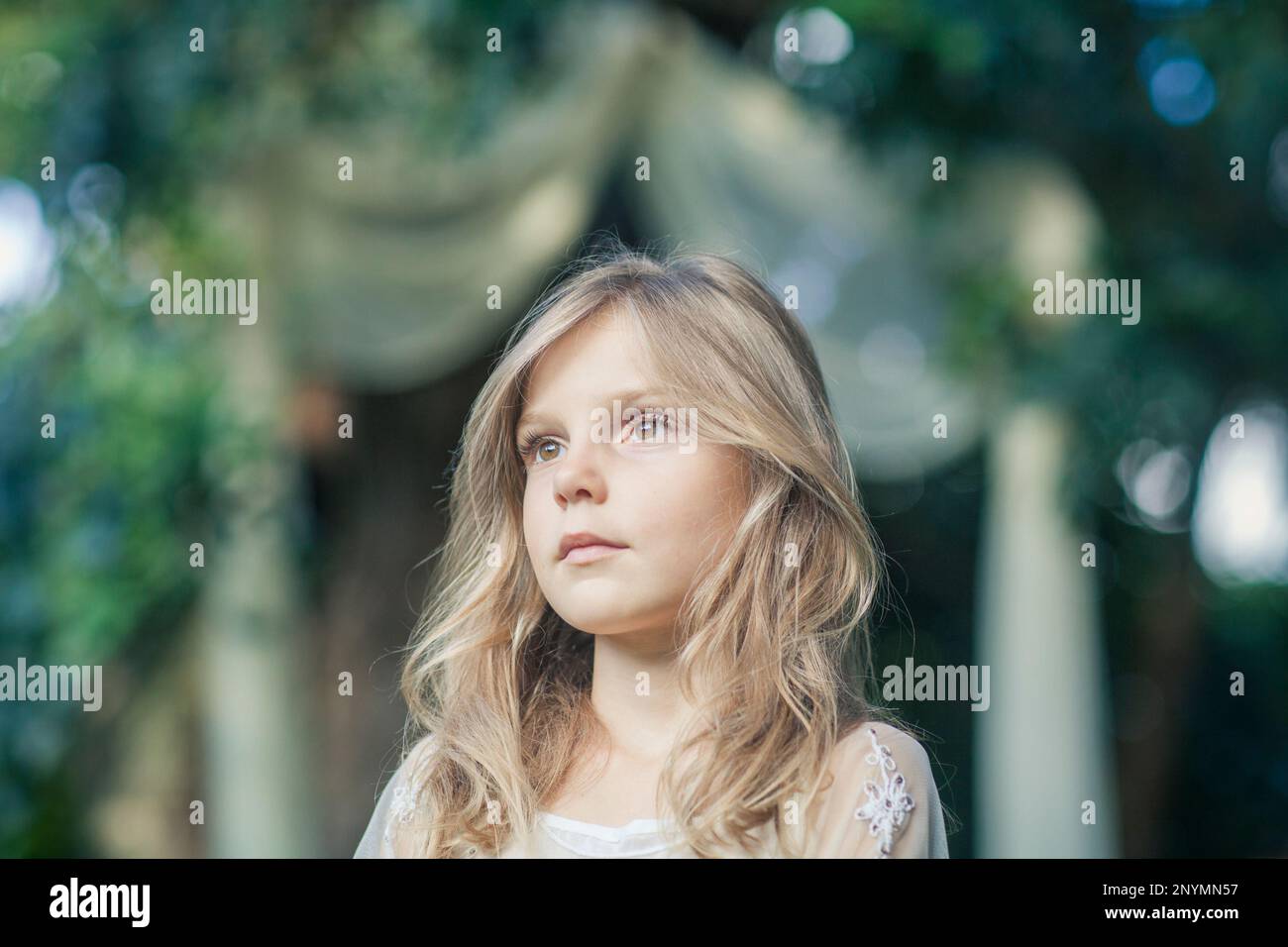 Little blond girl in elegant white dress with dreamy fabric arch