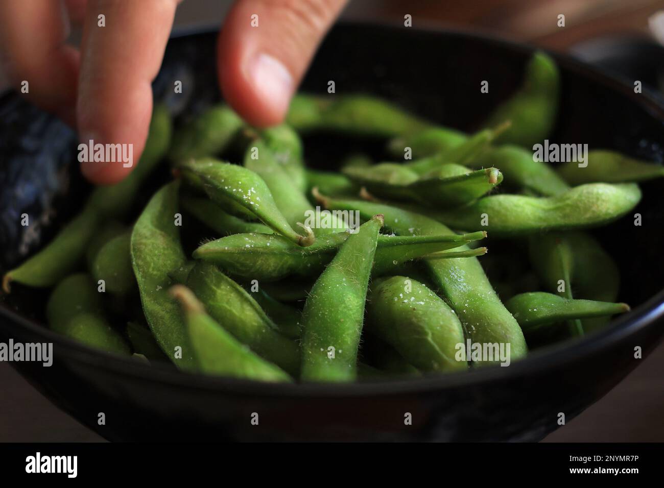 A man eating salted edamame from a black bowl Stock Photo Alamy