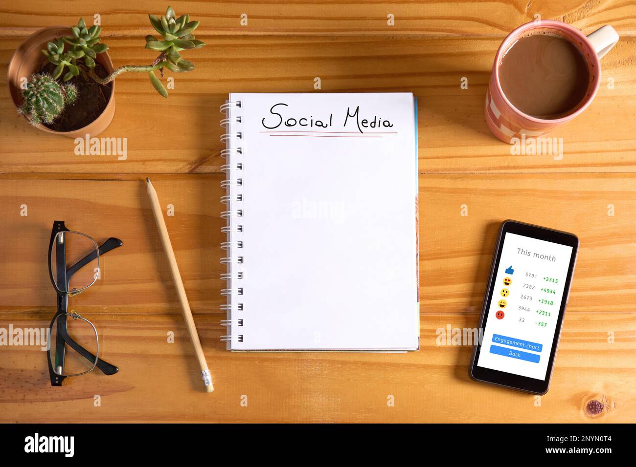Top view of notebook on table with 'Social media' text on blank page and mobile phone with icons showing positive report of engagement on the screen. Stock Photo