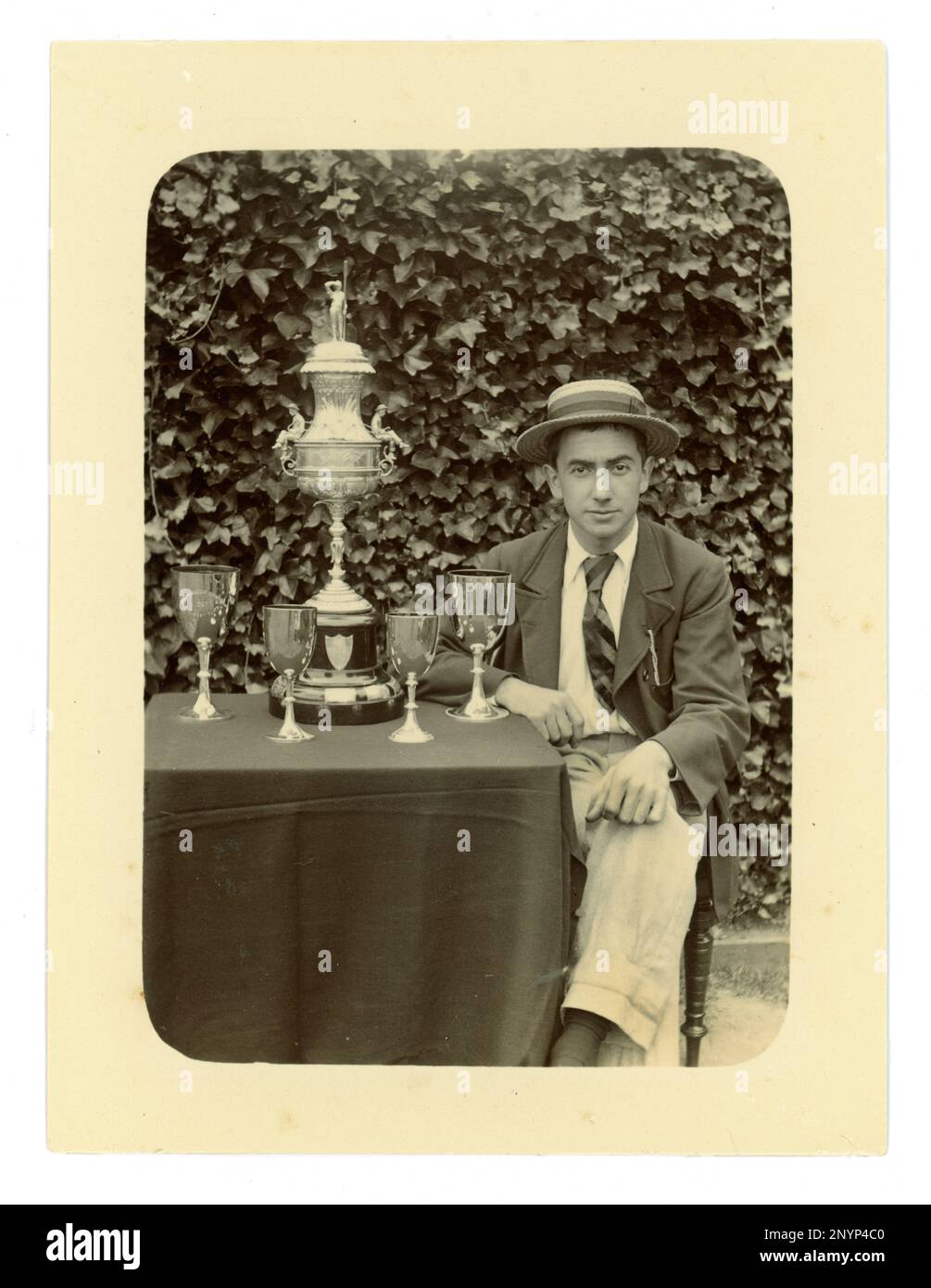 Original Victorian photograph of gent, wearing a jacket, club tie and boater. On a table there is displayed a large Worcester challenge vase, / regatta trophy for rowing, and other cups,  Possibly member of a coxed four crew. Worcester area, U.K.  circa 1897-1899 Stock Photo
