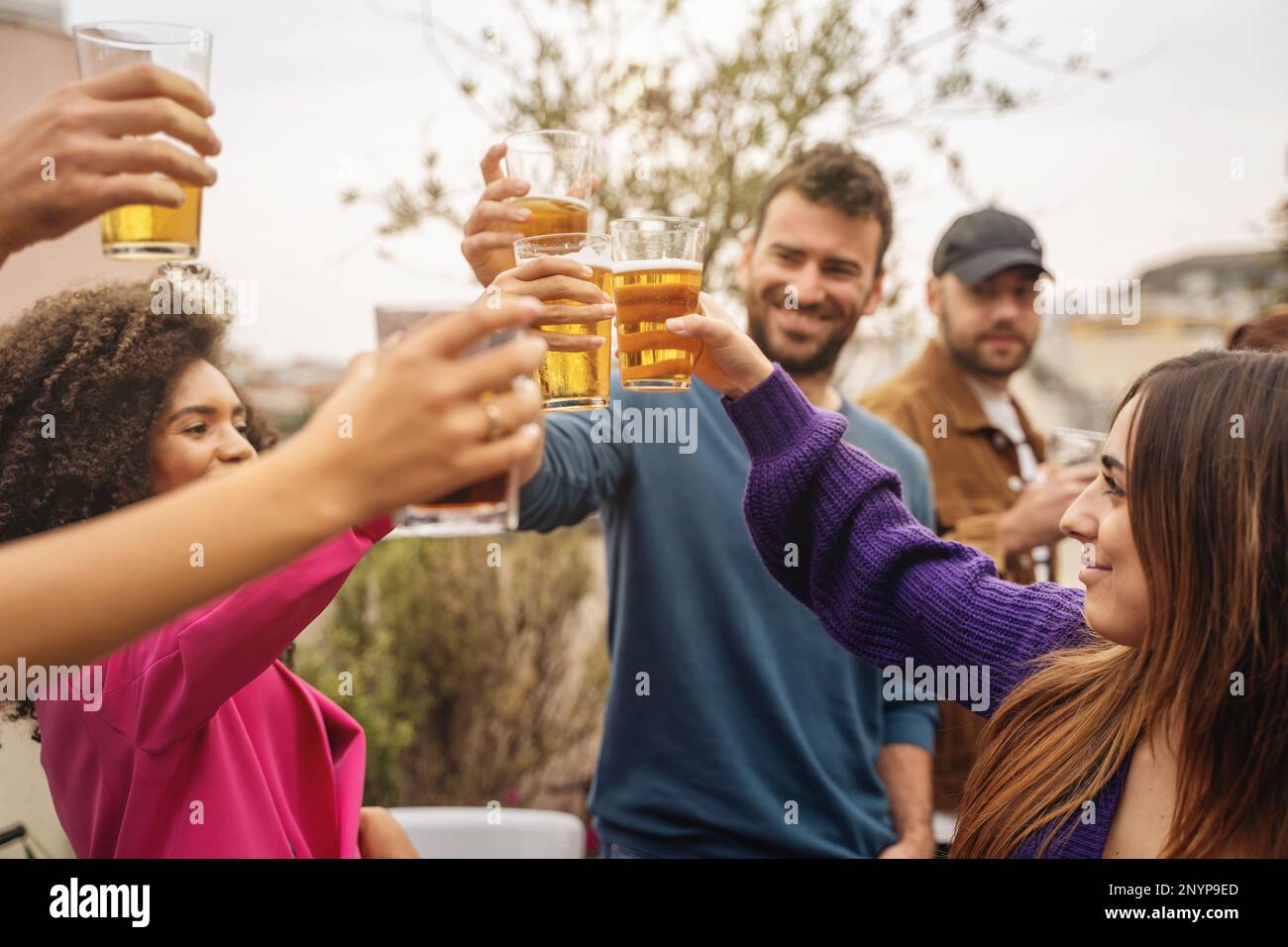 Multietnic student friends toast beers on hostel terrace celebrating end-of-year party - people lifestyle concept Stock Photo