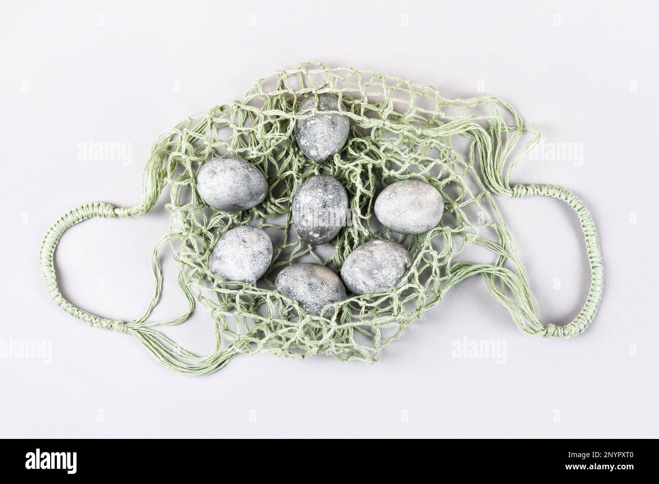 Grey Easter eggs in a green string bag on a grey background. Minimalism