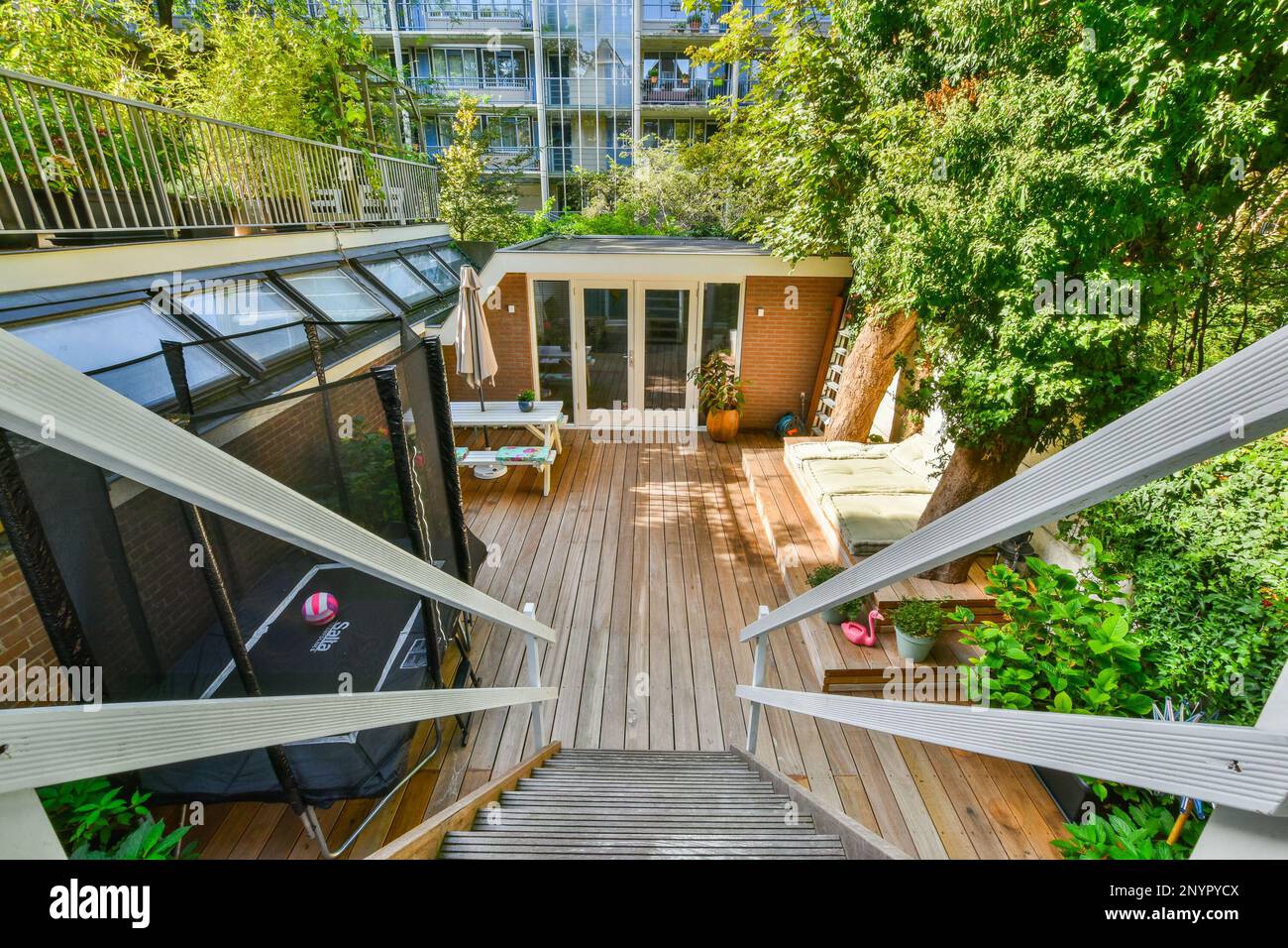 Amsterdam, Netherlands - 10 April, 2021: an outdoor living area with wood flooring and wooden stairs leading up to the upper level, surrounded by trees Stock Photo