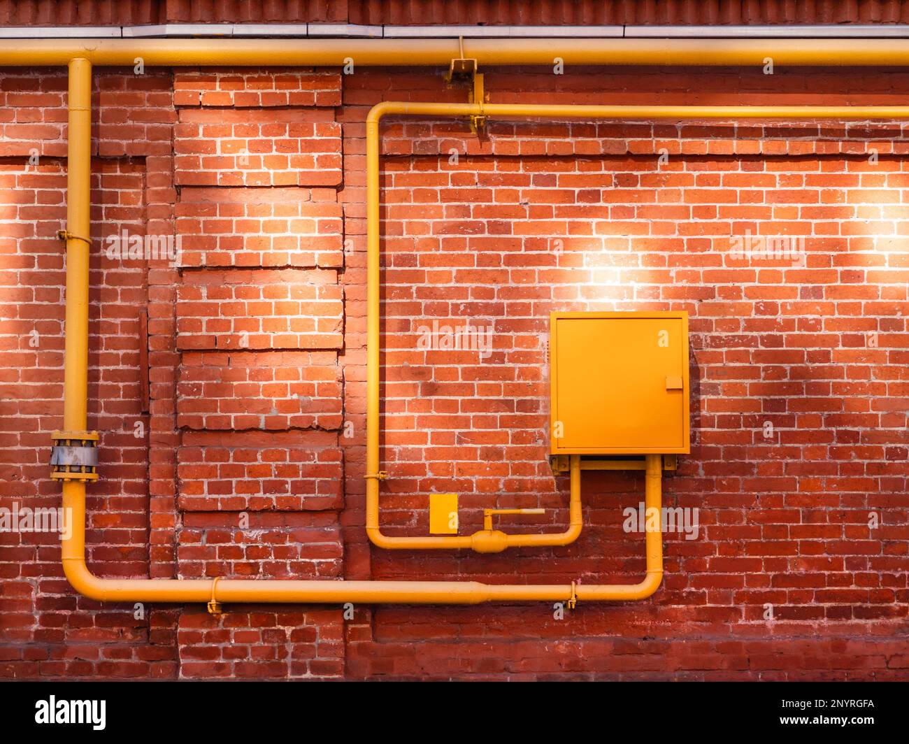 Red brick wall with yellow gas pipes and sunbeams. Old wall with sun reflections. Old building with shabby surface. Stock Photo