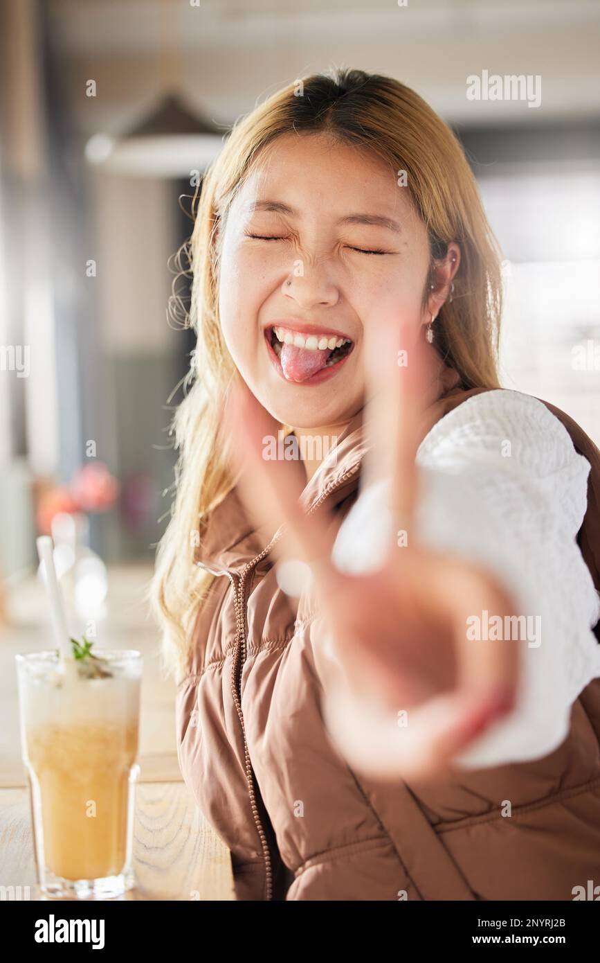 Peace, hand gesture and tongue with an asian woman in a coffee shop