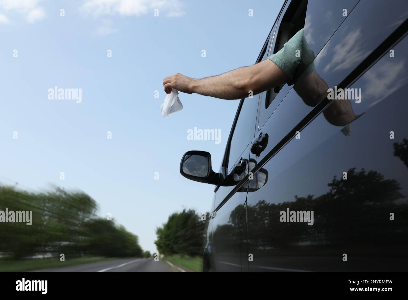 Driver throwing away wet wipe from car window, low angle view. Garbage