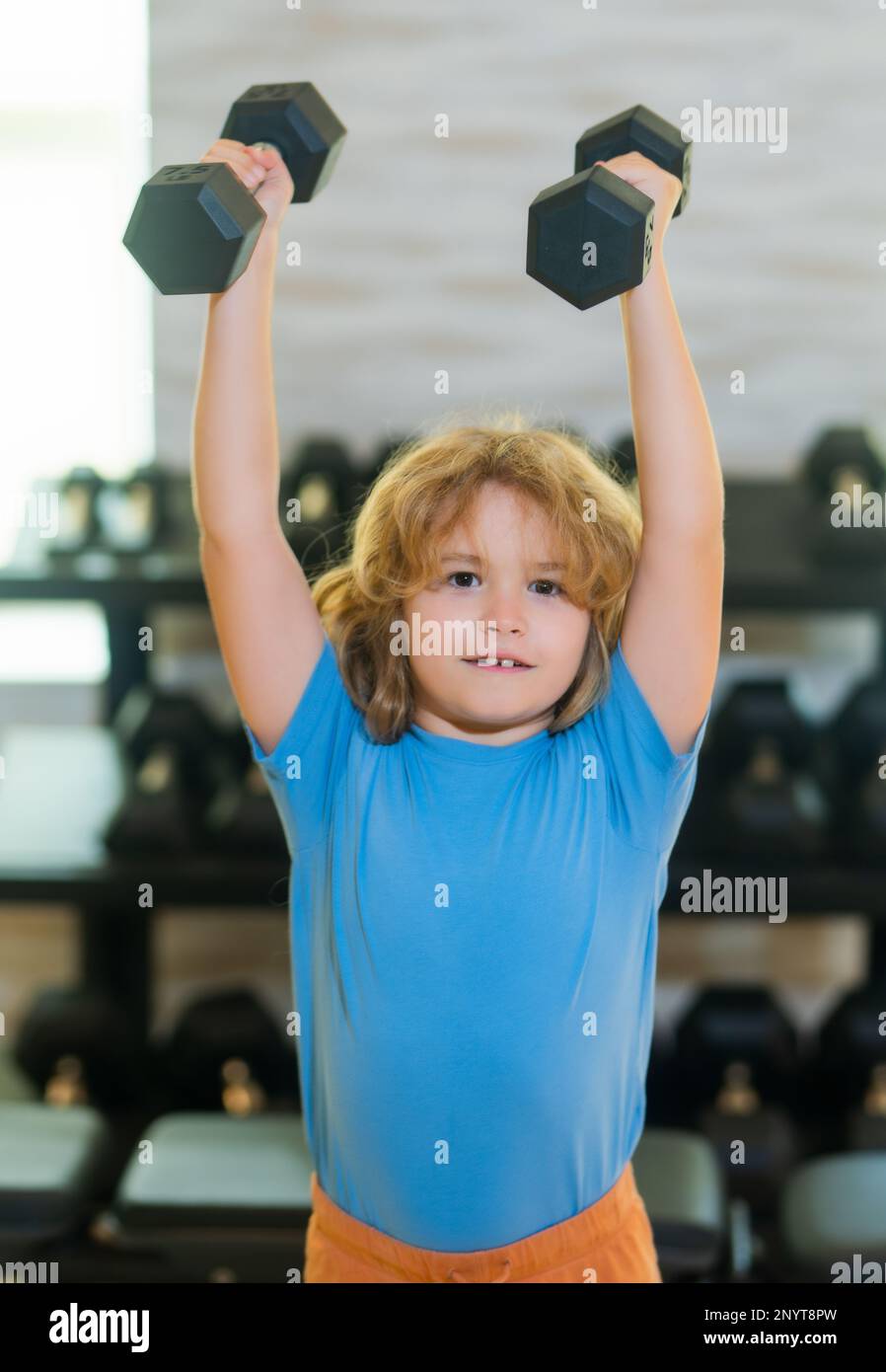 Child boy pumping up biceps muscles with dumbbell. Fitness kids with dumbbells Stock Photo