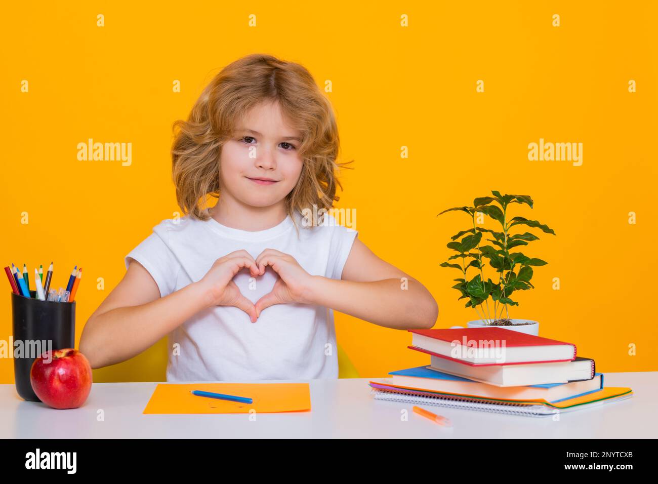 Pupil with love heard sign. Nerd pupil boy from elementary school with book isolated on yellow studio background. Smart genius intelligence kid ready Stock Photo
