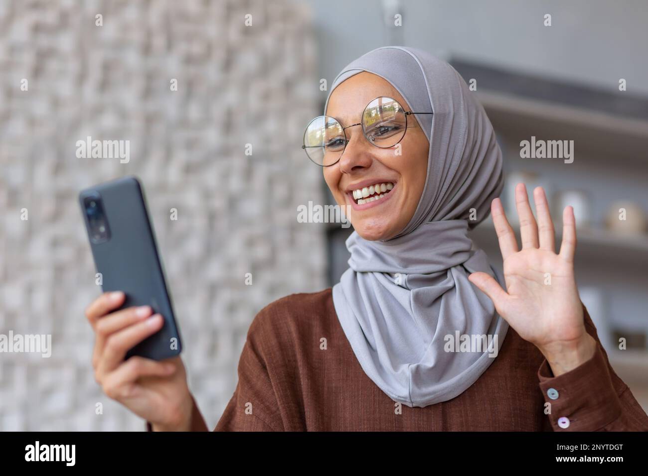 Young beautiful Muslim woman in hijab and glasses talking on video call ...