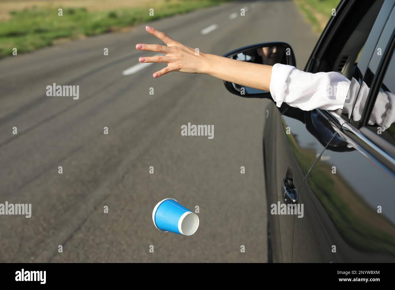 Driver throwing away paper cup from car window. Garbage on road Stock