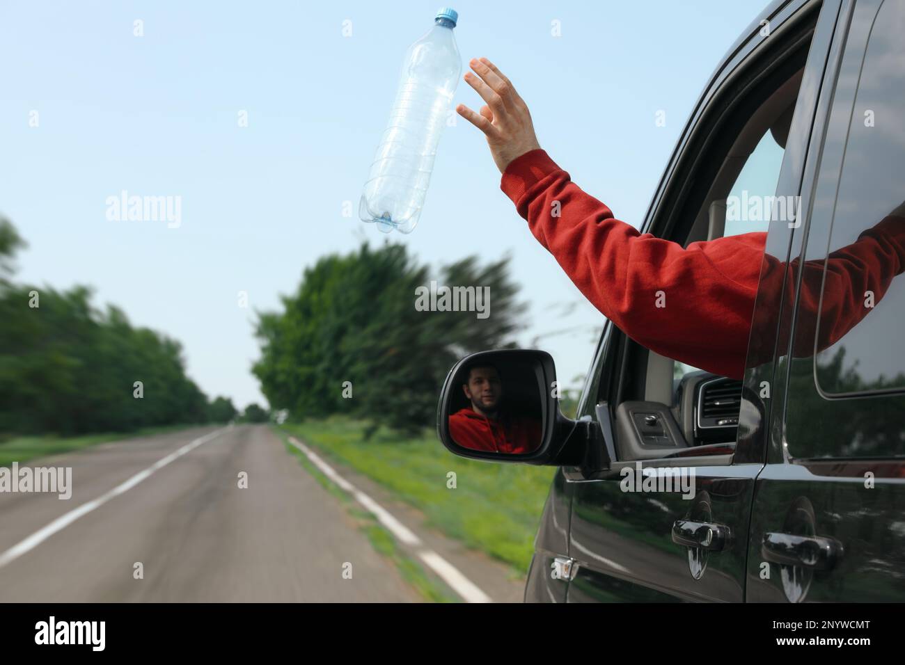 Driver throwing away plastic bottle from car window. Garbage on road