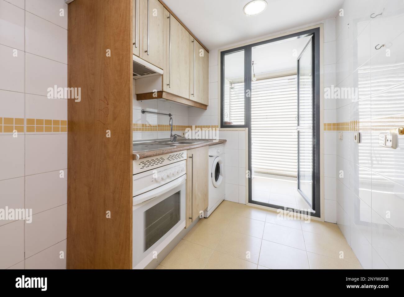 Kitchen furnished on one side with light wood furniture, integrated white appliances and exit to a drying terrace with glass door and aluminum structu Stock Photo
