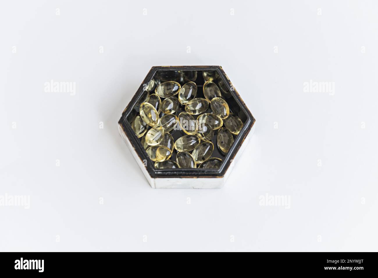 A hexagonal mother-of-pearl box with a black interior filled with pearls of a supreme liquid diet on a smooth white surface Stock Photo