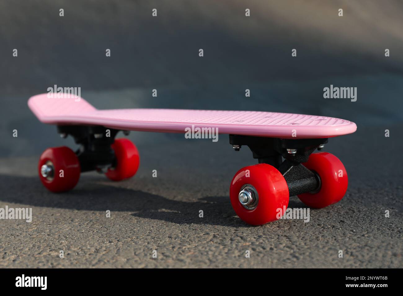 Modern pink skateboard with red wheels on asphalt road outdoors Stock Photo