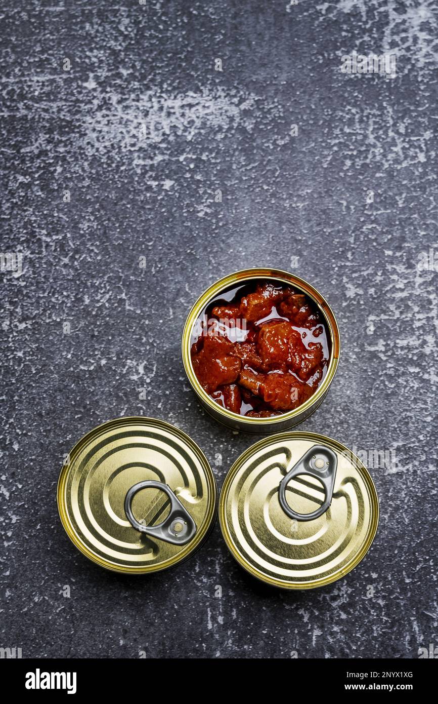 Three canned fish cans, one open circular on gray surface Stock Photo