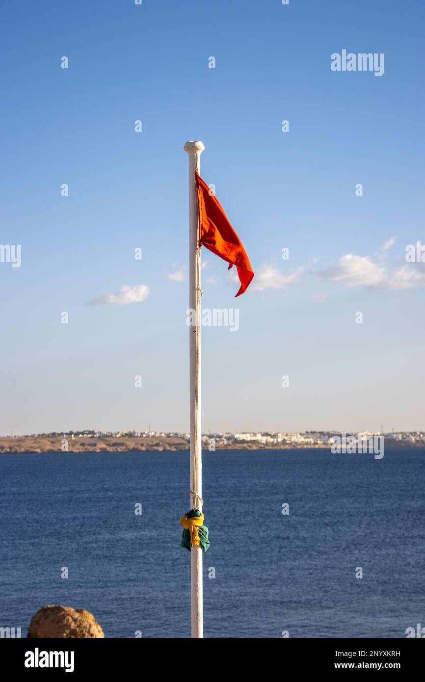 red warning flag and pole with the blue sea in the background Stock Photo