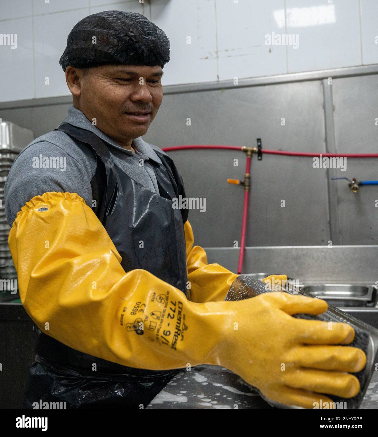 Dileep Kumar Choudhari, The Bridge Co. contractor, scrubs dishes at the Desert Winds dining facility at Ali Al Salem Air Base, Kuwait, Feb. 1, 2023. All members of the DFAC contribute to the base population’s overall health and wellness by providing nutritious meals that keep Airmen fit to fight. Stock Photo