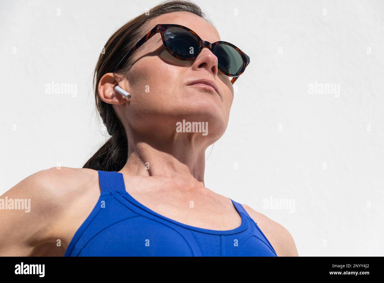 Close up of a sporty mid adult woman wearing wireless earphones while training in the sun Stock Photo