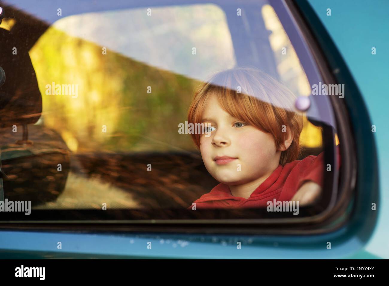 A young boy of eight or ten years old sits in a car behind glass. Car travel, train concept. Red