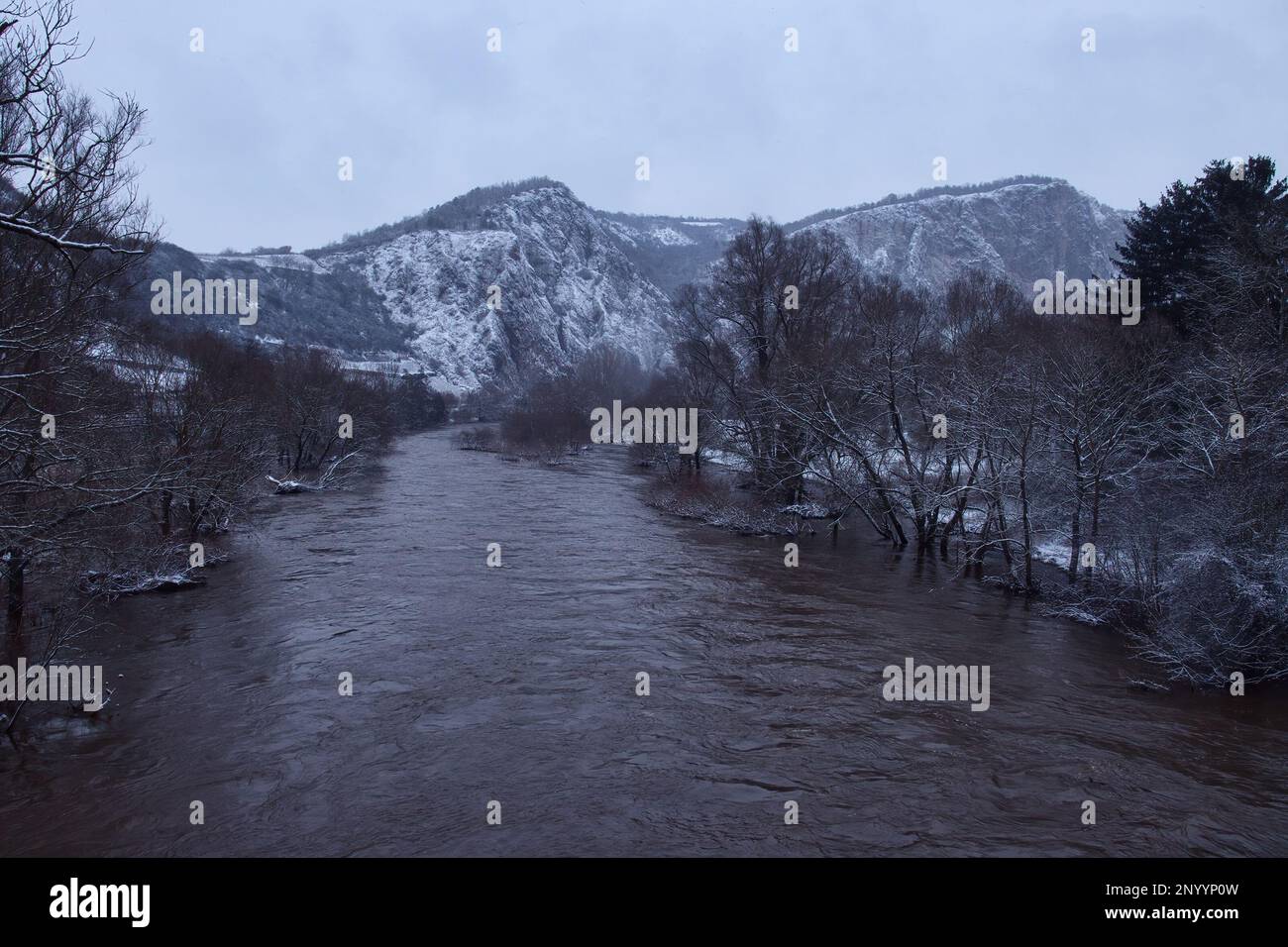 Nahe River surrounded by tree with Rotenfels mountains in the background on a dark, grey, snowy winter day in Rhineland Palatinate, Germany. Stock Photo