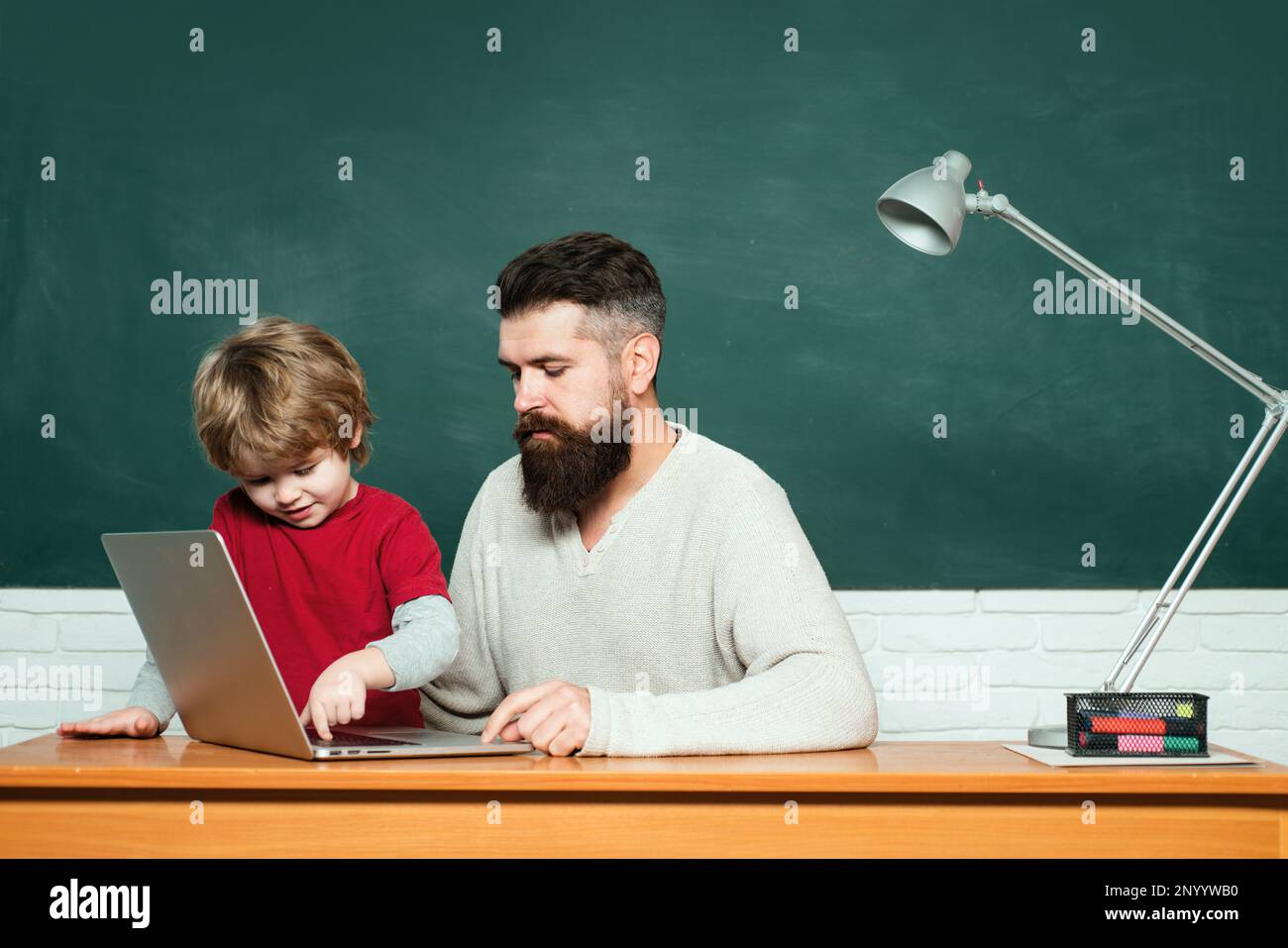 Elementary school teacher and student in classroom. Teacher and schoolboy using laptop in class. Chalkboard copy space. Father and son. Elementary Stock Photo