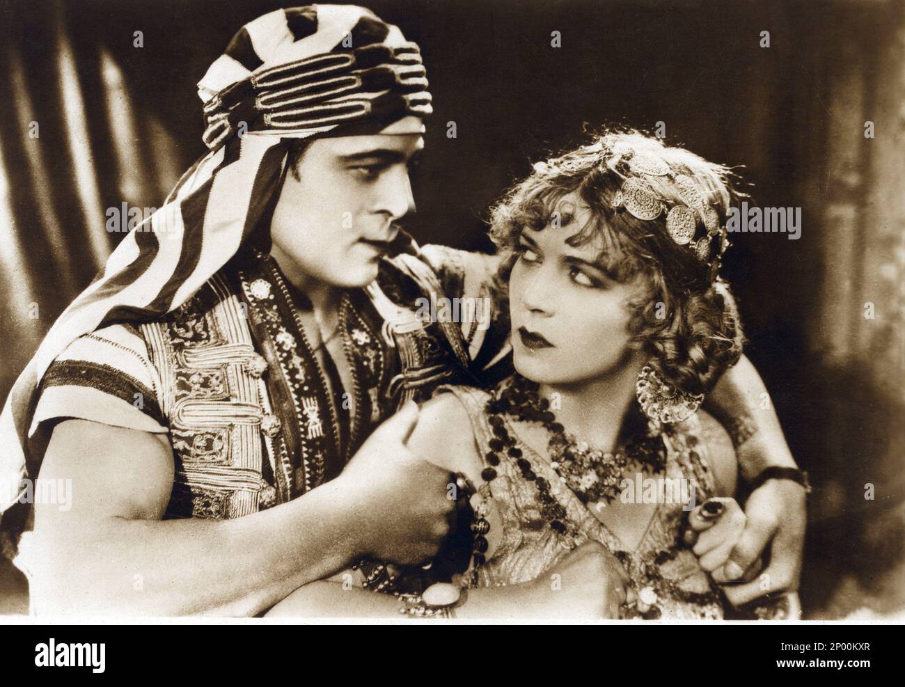 1926 , USA : The silent screen movie actor RUDOLPH VALENTINO ( born Rodolfo Guglielmi ,  1895 - 1926 ) with WILMA BANKY  in THE SON OF THE SHEIK ( Il figlio dello Sceicco ) by George Fitzmaurice , from the novel by Edith Maude Hull , Paramount Picture - CINEMA MUTO - RODOLFO - attore cinematografico - VILMA - LATIN LOVER - italoamericano - italo americano - italo-americano - emigrant - emigrante - italo-american - portrait - ritratto - turbante - turban  - arab - arabo - abbraccio - embrace - kiss - bacio - innamorati - lovers - amanti   ----  Archivio GBB Stock Photo