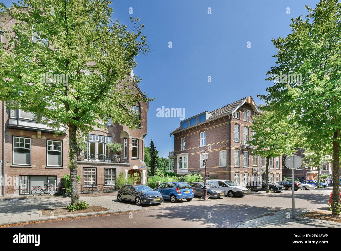 Amsterdam, Netherlands - 10 April, 2021: a city street with cars parked on the side and trees lining the street in front of buildings, all lined up against each other Stock Photo