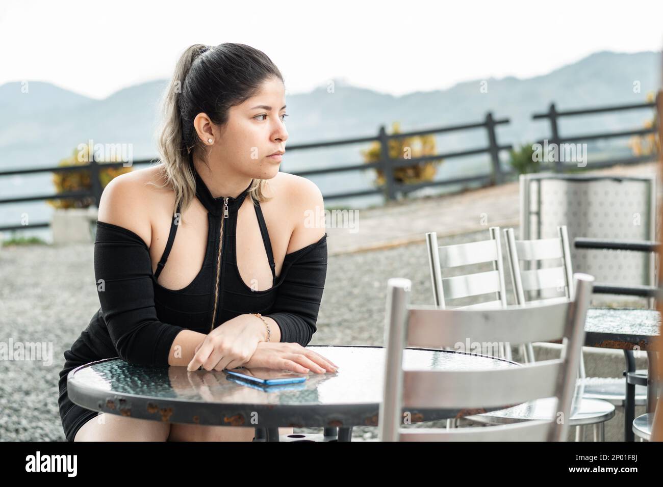 young latina woman, sitting waiting for the food she ordered, in an open-air restaurant Stock Photo