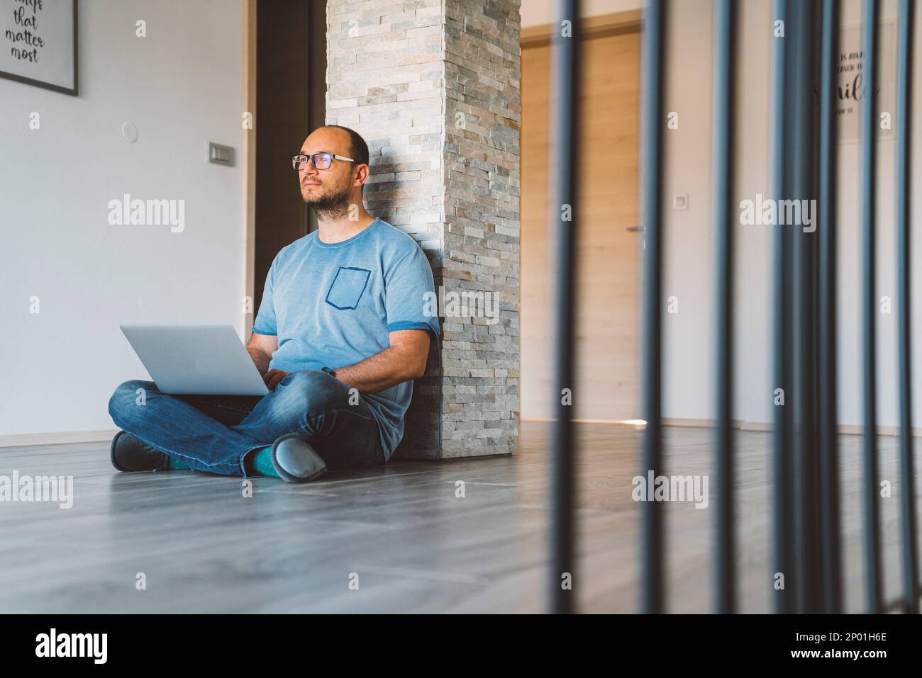 Man sitting with his legs crossed on the floor with laptop on his lap ...