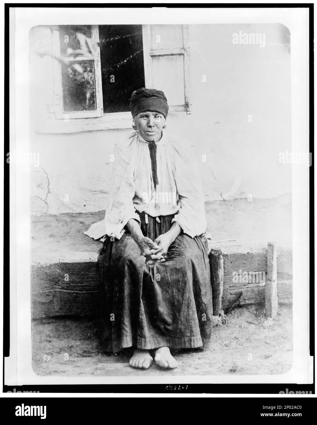 Old woman seated, outside house, full-length, Russia. Frank and Frances