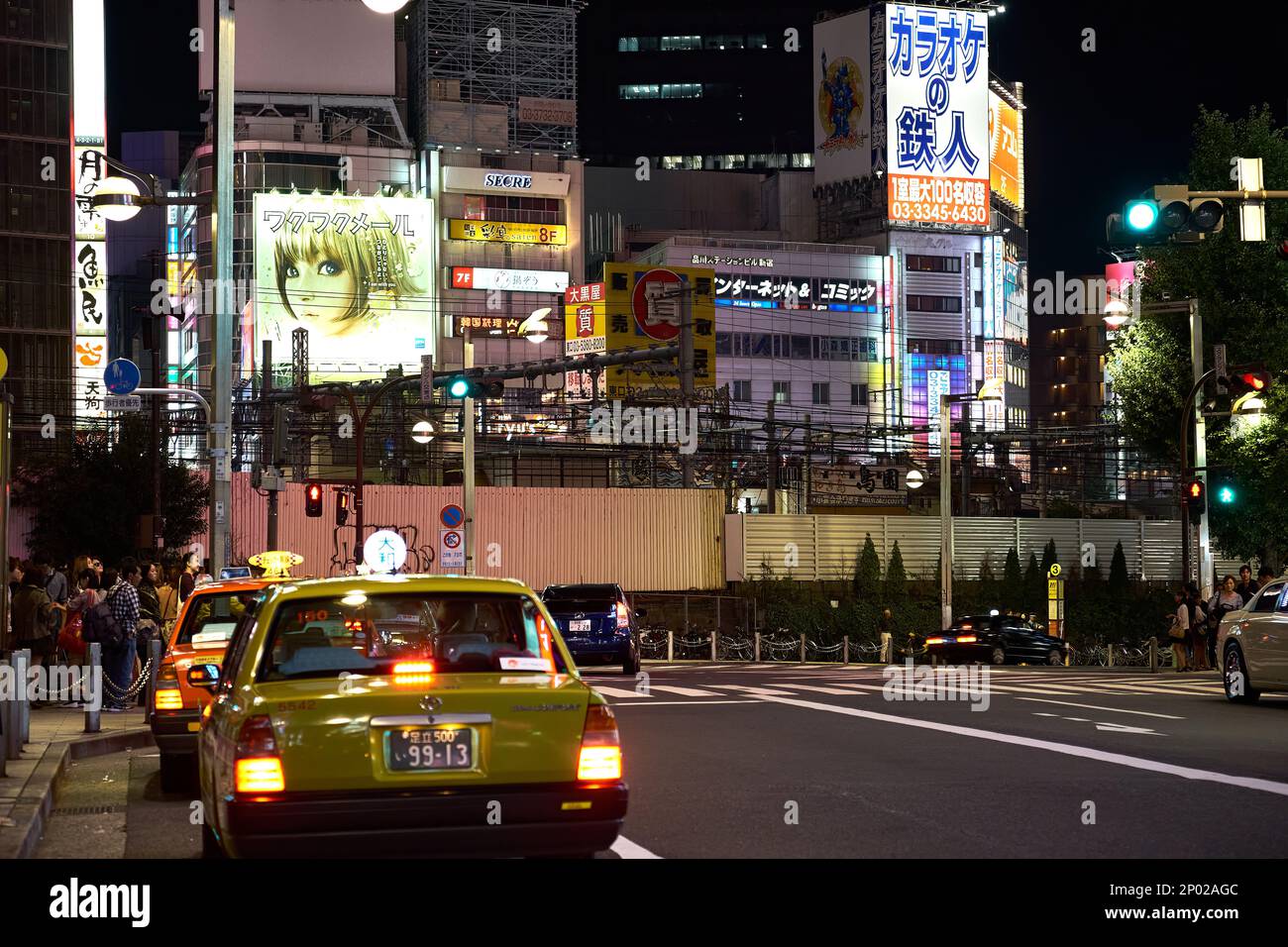 Japanese taxis waiting near a white zebra crossing with large neon advertising billboards on the surrounding buildings in Tokyo, Japan Stock Photo