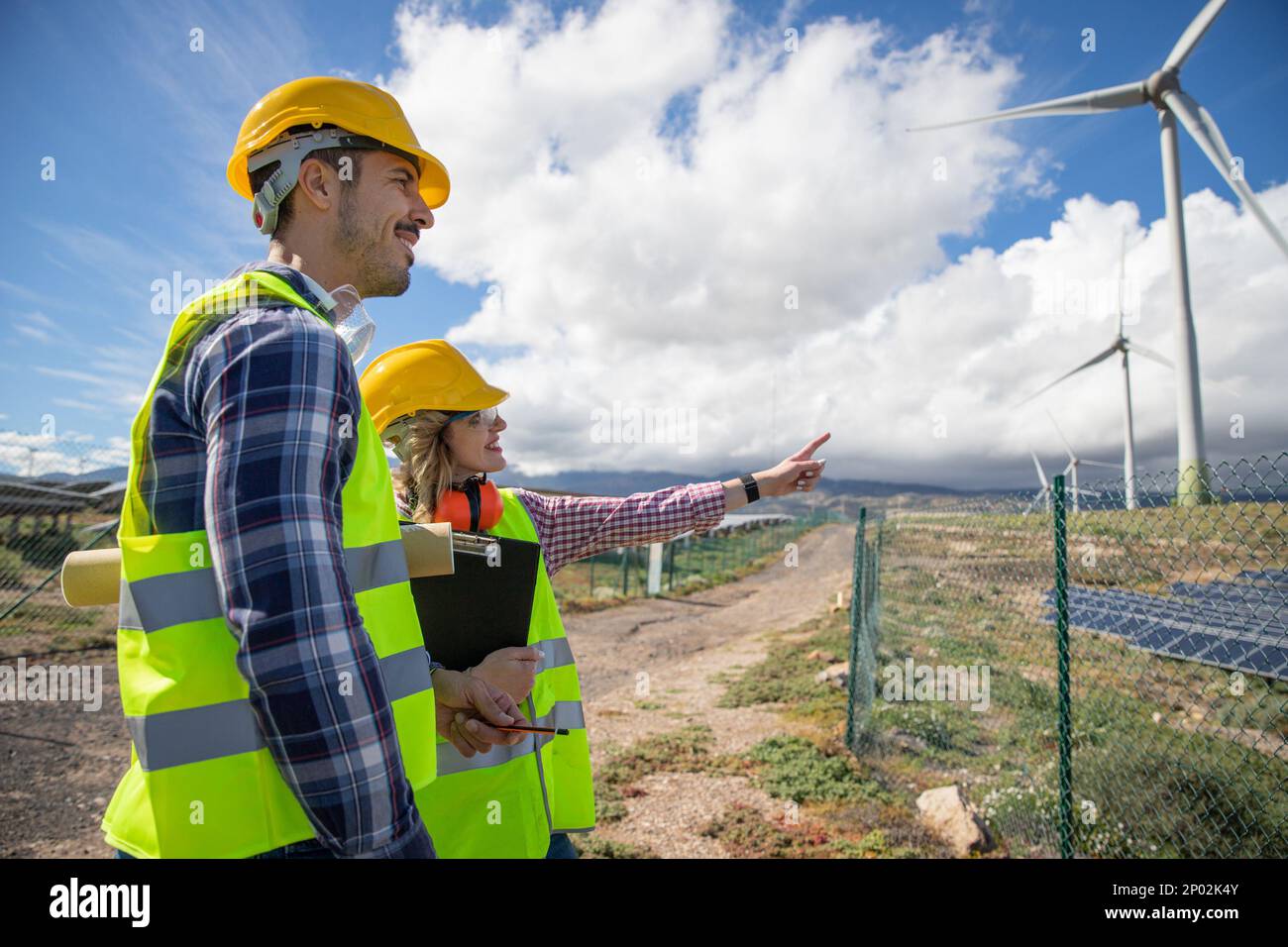 Two engineers are having a conversation while observing wind turbines, renewable energy concept. Stock Photo