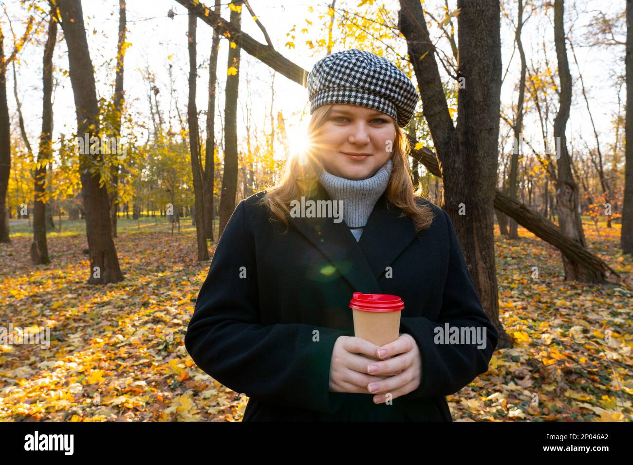 Autumn evening. Sunset. City Park. End of the working day. The girl is holding a cup of coffee in her hands. Walks in the open air. Unity with nature Stock Photo