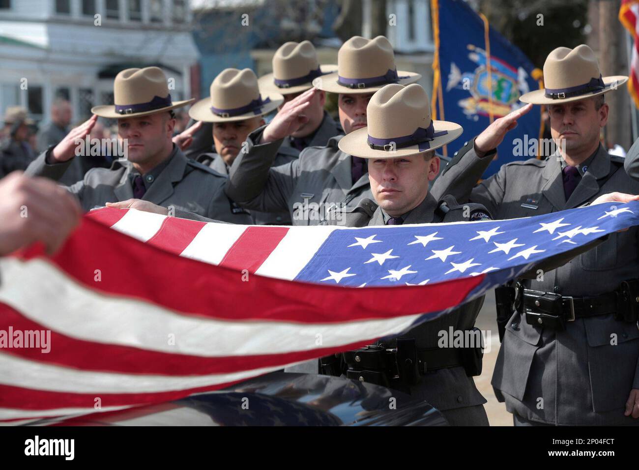 A New York State trooper helps to fold an American flag covering the